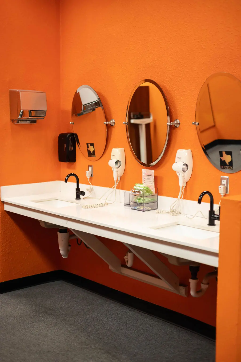 Locker room vanity area with mirrors and hair dryers at TX Fitness